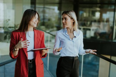 İki profesyonel kadın gündüz vakti gösterişli, çağdaş bir ofis binasının dışındaki tableti incelerken düşünceli bir tartışmaya giriyorlar..