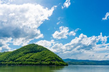 Sırbistan 'daki Porec Körfezi' nin sakin sularından yükselen yemyeşil tepe, parçalı bulutlu gökyüzünün altında, doğanın dingin güzelliğini yakalıyor.
