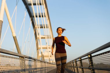 Güneş doğarken, kadın güven içinde köprüden geçiyor, sabah ışığını kucaklıyor ve canlandırıcı koşusu sırasında açık hava serinliyor.