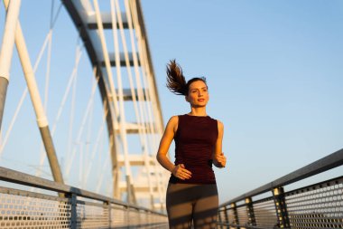 Güneş doğarken, kadın güven içinde köprüden geçiyor, sabah ışığını kucaklıyor ve canlandırıcı koşusu sırasında açık hava serinliyor.