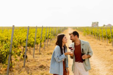 Batan güneşin sıcacık parıltıları altında, birkaç çift, üzüm bağlarında şarap yudumlarken kahkahalarını paylaşıyor, üzüm bağlarının arasında sevgi dolu anılar yaratıyor.