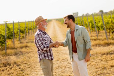İki adam üzüm bağları arasında anlamlı bir tartışmayı paylaşıyor, öğleden sonra güneşinin sıcaklığının tadını çıkarıyorlar, bağlılık ve bağcılık geleneğini sembolize ediyorlar