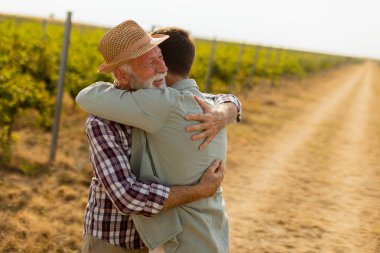 Sarmaşıkların yemyeşil sıraları arasında, neşeli bir kucaklama iki nesil arasında gerçekleşir, güneşli bir günde sevgi ve bağın bir anını yakalar
