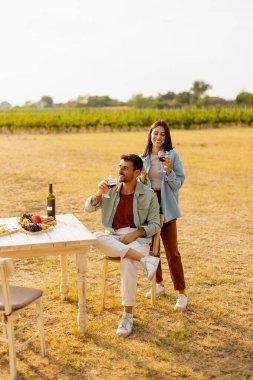 Güneşli bir üzüm bağının kırsal bir masasında, şarabın ve gurme atıştırmalıkların tadını çıkaran bir çift. Bereketli sarmaşıklar ve akşamın sıcaklığıyla çevrili kahkahalar ve neşeyi paylaşıyorlar.