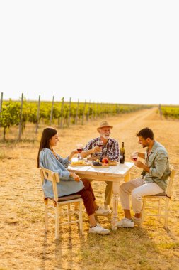 Yeşillik sarmaşıkların arasında, üç arkadaş keyifli bir öğleden sonra geçirir, şarabın ve sohbetin tadını çıkarırlar, doğanın güzellikleriyle çevrelenmiş bir şekilde. 