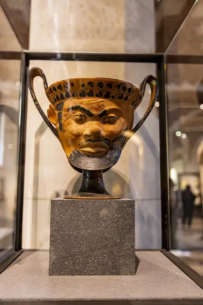 stock image Paris, France - April 10, 2023: Ancient Greek kantharos - vase for drinking wine in shape of Satyr head from Louvre museum in Paris, France. It is a national art museum founded at 1793.