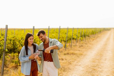 Batan güneşin sıcacık parıltıları altında, birkaç çift, üzüm bağlarında şarap yudumlarken kahkahalarını paylaşıyor, üzüm bağlarının arasında sevgi dolu anılar yaratıyor.