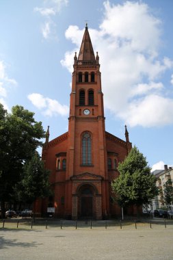 Berlin-Schneberg 'deki On İki Havari Kilisesi' nin çarpıcı manzarasında kırmızı tuğla mimarisi ve berrak gökyüzü sergileniyor. Şehir yeşilliğinin ortasındaki tarihi güzelliğini vurguluyor. 
