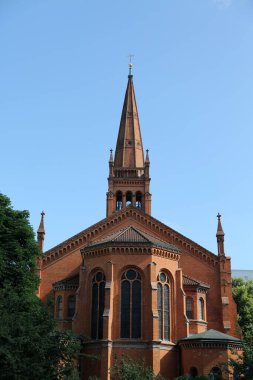 Berlin-Schneberg 'deki On İki Havari Kilisesi' nin çarpıcı manzarasında kırmızı tuğla mimarisi ve berrak gökyüzü sergileniyor. Şehir yeşilliğinin ortasındaki tarihi güzelliğini vurguluyor. 