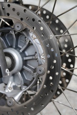 Motosikletin tekerleği döner, fren diskinin yakın çekimini ortaya çıkarır, delikler şeklinde vurgulanır, metal teller yumuşak güneş ışığı altında parlarken
