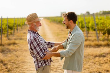 İki adam üzüm bağları arasında anlamlı bir tartışmayı paylaşıyor, öğleden sonra güneşinin sıcaklığının tadını çıkarıyorlar, bağlılık ve bağcılık geleneğini sembolize ediyorlar