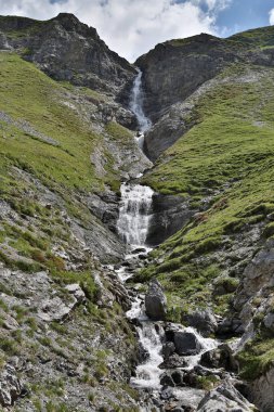 Lombardy, İtalya 'daki Braulio Vadisi' nin kayalık yamaçlarında bulutların öptüğü parlak mavi gökyüzünün altında görkemli şelaleler.