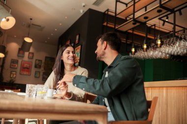 İki arkadaş büyüleyici bir kafede kahkaha ve sıcak içecekleri paylaşıyor, güneşli bir günde bağlantı ve neşeyi kutlayan davetkar bir ortam yaratıyorlar.