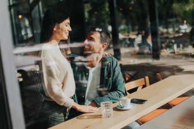 İki arkadaş büyüleyici bir kafede kahkaha ve sıcak içecekleri paylaşıyor, güneşli bir günde bağlantı ve neşeyi kutlayan davetkar bir ortam yaratıyorlar.