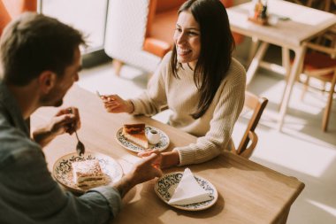 Sıcak, davetkar bir kafede, öğleden sonra güneşlenirken, bir çift kahkaha ve lezzetli ikramlar paylaşır, kahvenin ve hamur işlerinin tadını çıkarır..