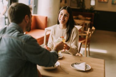 Bir çift, parlak bir kafedeki ahşap bir masada oturup kahkahalarını ve kokteyllerini paylaşıyor. Sıcak güneş ışığı sıcacık bir parıltı saçar, neşeli anlarını ve lezzetli atıştırmalıklarını güçlendirir..