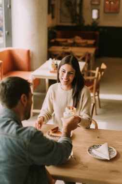 Bir çift, parlak bir kafedeki ahşap bir masada oturup kahkahalarını ve kokteyllerini paylaşıyor. Sıcak güneş ışığı sıcacık bir parıltı saçar, neşeli anlarını ve lezzetli atıştırmalıklarını güçlendirir..