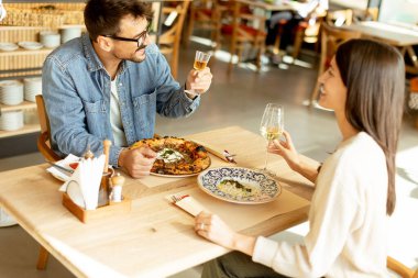 İki birey, rahatlamış bir restoran atmosferine dalmış, ahşap bir masada içkilerinin tadını çıkarırken sohbet ve kahkahaların derinliklerinde....