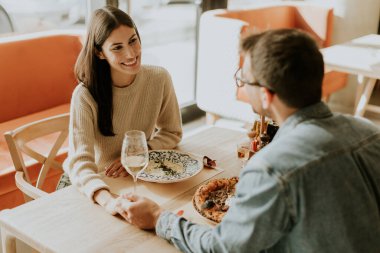 Bir çift, rahat bir restoran atmosferinde, ahşap bir masada otururken lezzetli yemekler ve kahkahalar paylaşarak keyifli bir akşam geçirir..