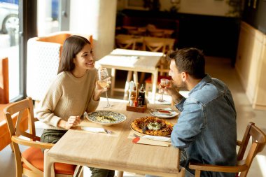 İki birey, rahatlamış bir restoran atmosferine dalmış, ahşap bir masada içkilerinin tadını çıkarırken sohbet ve kahkahaların derinliklerinde....