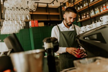 Şık bir kafe içinde, yetenekli bir barista, düzenli düzenlenmiş cam süslemeler ve canlı dekorlarla çevrili lezzetli içecekler hazırlamaya odaklanıyor, müşteriler için sıcak bir ortam yaratıyor..