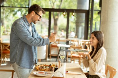 Neşeli bir çift, güzel bir kafe masasında oturur, güzel bir yemek ve güneşli bir atmosferle çevrili akıllı bir telefondan anı yakalarken gülümserler.