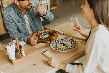 İki birey, rahatlamış bir restoran atmosferine dalmış, ahşap bir masada içkilerinin tadını çıkarırken sohbet ve kahkahaların derinliklerinde....