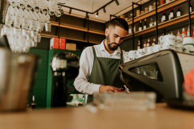 Şık bir kafe içinde, yetenekli bir barista, düzenli düzenlenmiş cam süslemeler ve canlı dekorlarla çevrili lezzetli içecekler hazırlamaya odaklanıyor, müşteriler için sıcak bir ortam yaratıyor..