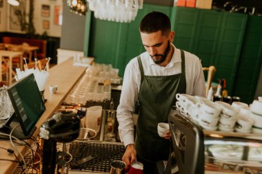 Sıcak ve davetkar bir kafede, kendini adamış bir barista kahve bardağına ustalıkla süt dökerek müşteriler için hoş bir deneyim yaratıyor..