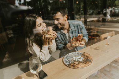 Bir çift hoş bir şekilde büyüleyici bir kafede pizza dilimleri ile şımarır. Parlak, havadar bir ortam ve her ısırığın tadını birlikte çıkarırlar. 