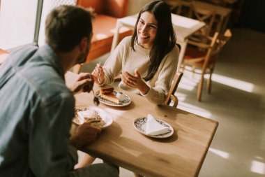 Sıcak, davetkar bir kafede, öğleden sonra güneşlenirken, bir çift kahkaha ve lezzetli ikramlar paylaşır, kahvenin ve hamur işlerinin tadını çıkarır..