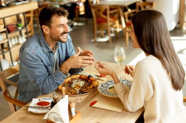 Parlak bir restoranda leziz mutfakların tadını çıkarırken neşeli bir sohbete girişen bir çift, keyifli bir yemek eşliğinde kahkaha ve iletişim anlarını paylaşıyor..