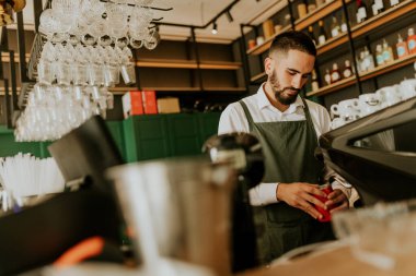 Şık bir kafe içinde, yetenekli bir barista, düzenli düzenlenmiş cam süslemeler ve canlı dekorlarla çevrili lezzetli içecekler hazırlamaya odaklanıyor, müşteriler için sıcak bir ortam yaratıyor..