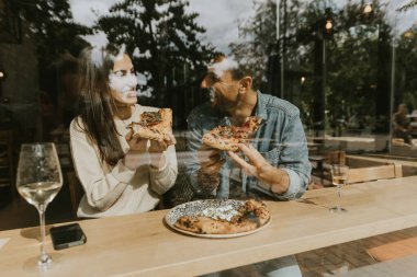 Bir çift hoş bir şekilde büyüleyici bir kafede pizza dilimleri ile şımarır. Parlak, havadar bir ortam ve her ısırığın tadını birlikte çıkarırlar. 