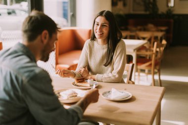 Sıcak, davetkar bir kafede, öğleden sonra güneşlenirken, bir çift kahkaha ve lezzetli ikramlar paylaşır, kahvenin ve hamur işlerinin tadını çıkarır..
