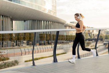 Sabahın erken saatlerinde bir kadın, çağdaş mimariyle çevrili şık bir şehir yolunda koşar ve sağlıklı bir yaşam tarzına olan bağlılığını gösterir..