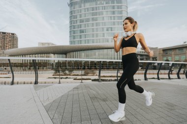 Şık bir şehir yolunda koşan bir kadın, çağdaş mimari ve sakin bir atmosferle çevrili iken ferahlatıcı açık havayı kucaklıyor.