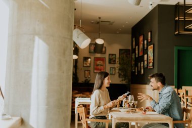 Parlak bir restoranda leziz mutfakların tadını çıkarırken neşeli bir sohbete girişen bir çift, keyifli bir yemek eşliğinde kahkaha ve iletişim anlarını paylaşıyor..