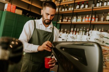 Şık bir kafe içinde, yetenekli bir barista, düzenli düzenlenmiş cam süslemeler ve canlı dekorlarla çevrili lezzetli içecekler hazırlamaya odaklanıyor, müşteriler için sıcak bir ortam yaratıyor..