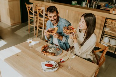 Birkaç arkadaş, üzerinde taze malzemeler olan ve yanında bir bardak şarapla birlikte mükemmel pişmiş pizzanın tadını çıkaran bir kır masasının üzerinde bir anı paylaşıyor..