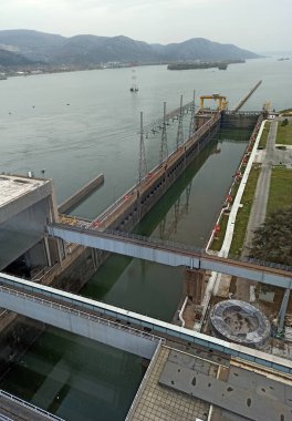 Cerdap 1 hidroelektrik santralinde, yüksek vinçler ve sağlam yapılar birlikte çalışarak, teknoloji ve dingin Tuna Nehri manzarası arasındaki sinerjiyi yansıtıyor.