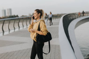 Güneş ufuk çizgisinden yükselirken, parlak sarı kazak giymiş genç bir kadın nehir boyunca yürür, akıllı telefonuyla müzik dinlerken büyülenir..