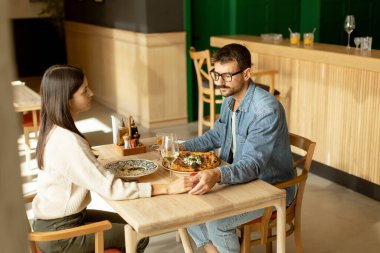 Parlak bir restoranda leziz mutfakların tadını çıkarırken neşeli bir sohbete girişen bir çift, keyifli bir yemek eşliğinde kahkaha ve iletişim anlarını paylaşıyor..