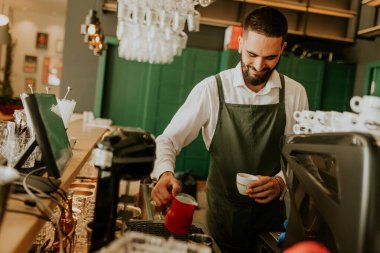 Sıcak ve davetkar bir kafede, kendini adamış bir barista kahve bardağına ustalıkla süt dökerek müşteriler için hoş bir deneyim yaratıyor..