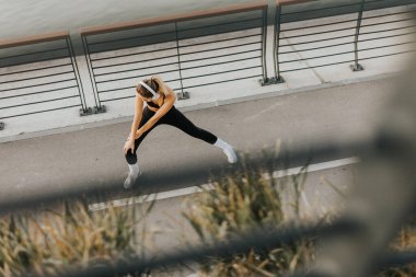 Sabahın sessizliğinde, atletik giyinen genç bir kadın şehir yolunda geriniyor, kulaklıkları takılı, vücuduna egzersiz için enerji vermeye ya da koşmaya odaklanıyor..