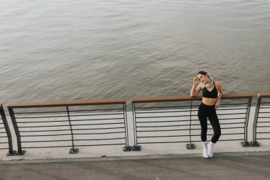 Suyun kenarında kararlı bir sporcu, hava kararırken ve nehir yumuşak renkleri yansıtırken o anın dinginliğini kucaklayarak esnemek için durur.. 