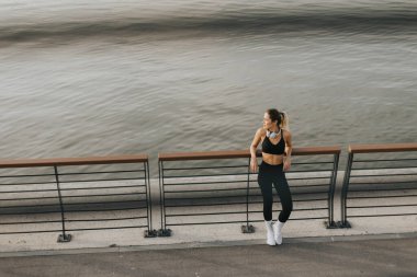 Suyun kenarında kararlı bir sporcu, hava kararırken ve nehir yumuşak renkleri yansıtırken o anın dinginliğini kucaklayarak esnemek için durur.. 