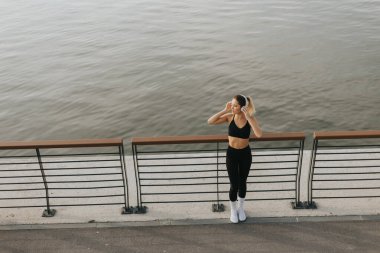 Suyun kenarında kararlı bir sporcu, hava kararırken ve nehir yumuşak renkleri yansıtırken o anın dinginliğini kucaklayarak esnemek için durur.. 