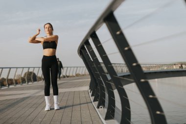 Güneşin altında ışıl ışıl genç bir kadın, canlı bir şehir manzarasında, canlı bir korkuluğa, sağlıklı ve zinde olmaya kendini adamış, güvenli bir şekilde kollarını uzatır..