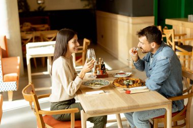 İki birey, rahatlamış bir restoran atmosferine dalmış, ahşap bir masada içkilerinin tadını çıkarırken sohbet ve kahkahaların derinliklerinde....